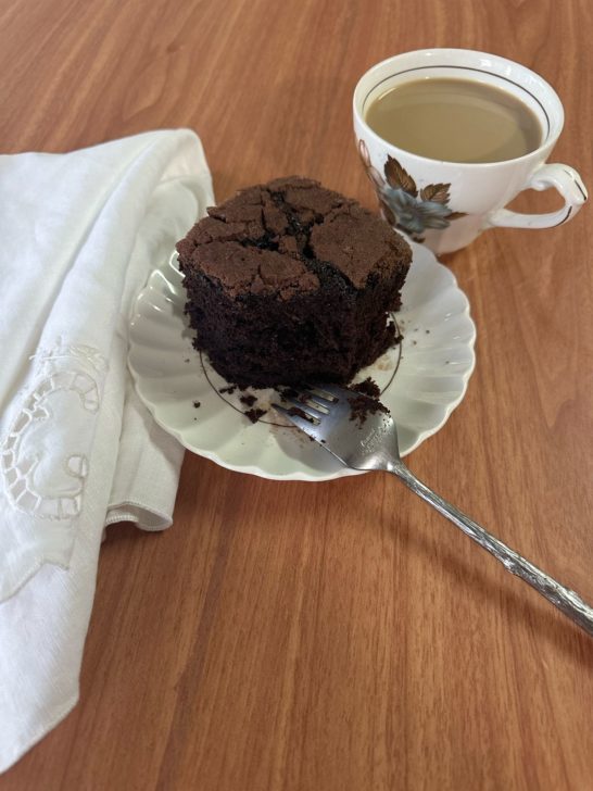The best chocolate cake for passover on a white plate with a fork and a cup of coffee and a white napkin nearby